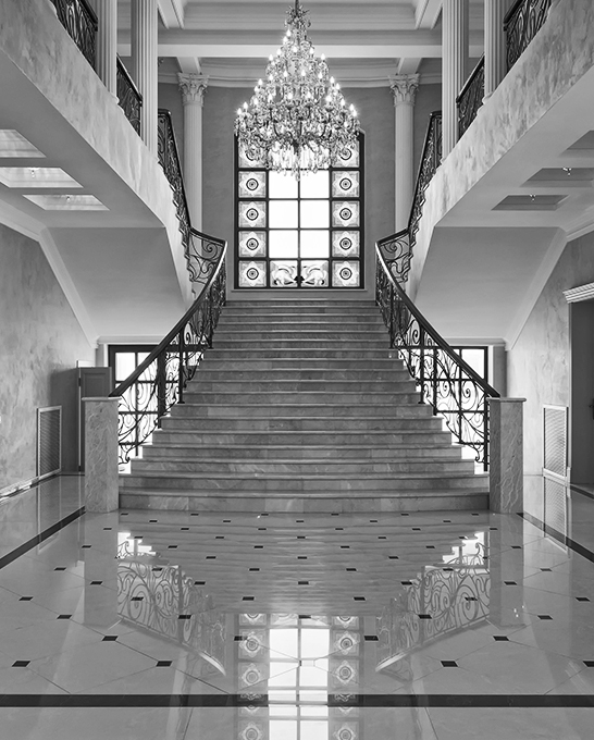 A classic grand staircase with chandelier in a lobby of a luxury mansion